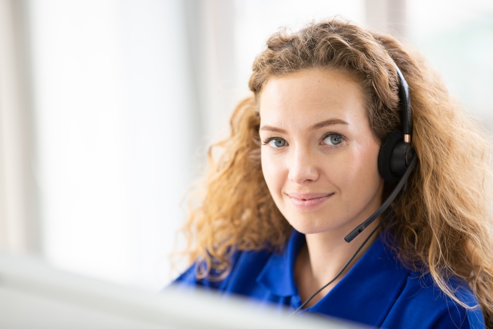 Young friendly operator woman agent with headsets working in a call centre.